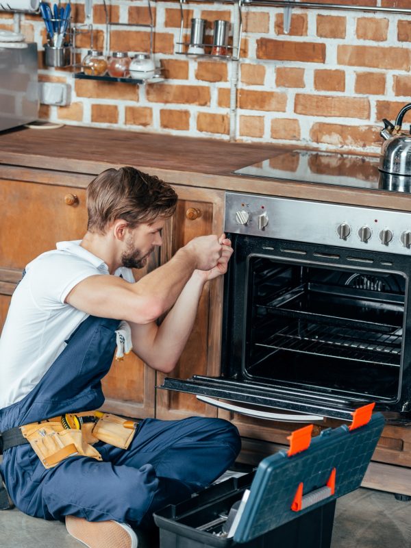 high angle view of young repairman fixing oven in kitchen